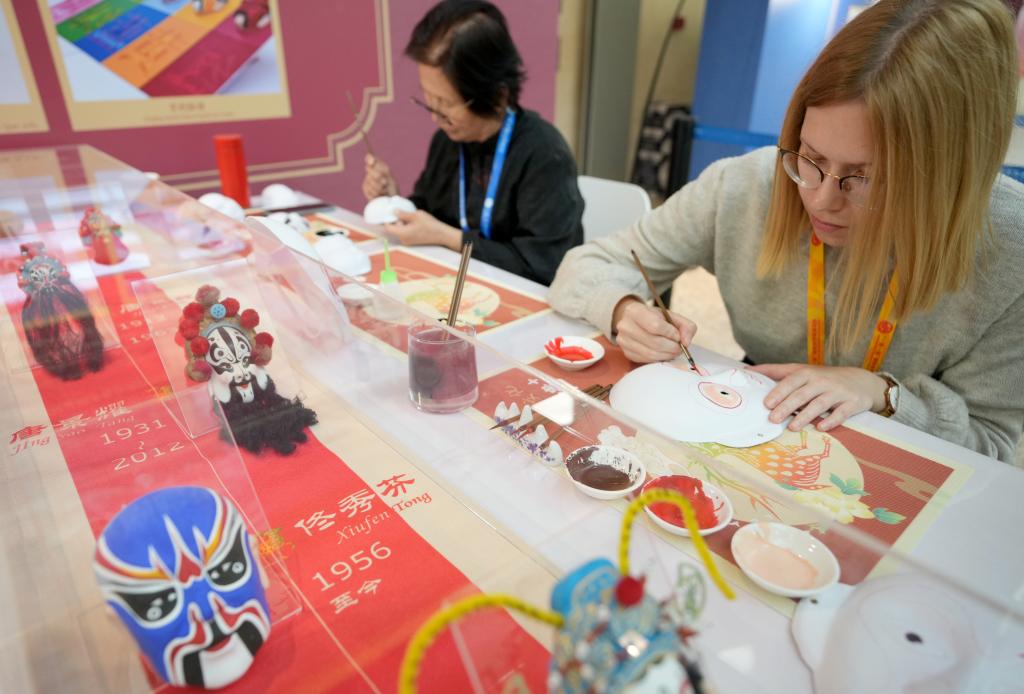 10月16日，在第三屆“一帶一路”國際合作高峰論壇新聞中心，來自比利時的記者（右）體驗畫京劇臉譜。新華社記者 王毓國 攝