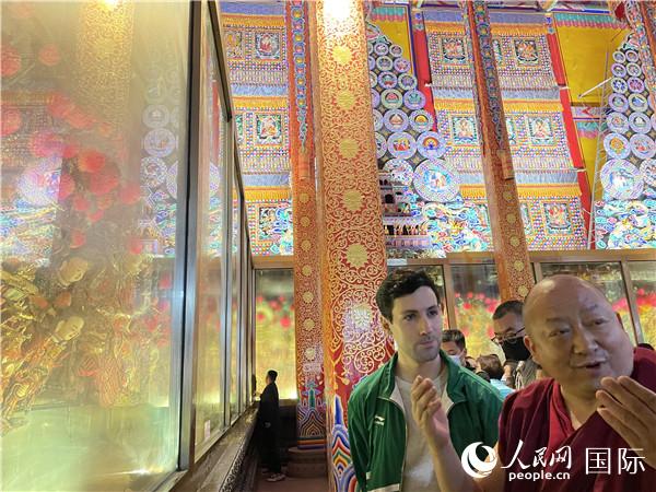 7月25日，省級非物質文化遺產項目塔爾寺酥油花的代表性傳承人朋措堅參（右）在塔爾寺酥油花館講解酥油花的制作過程。人民網 謝瑩攝