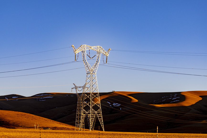 阿里地區的曠野上，電力鐵塔在夕陽下熠熠生輝。